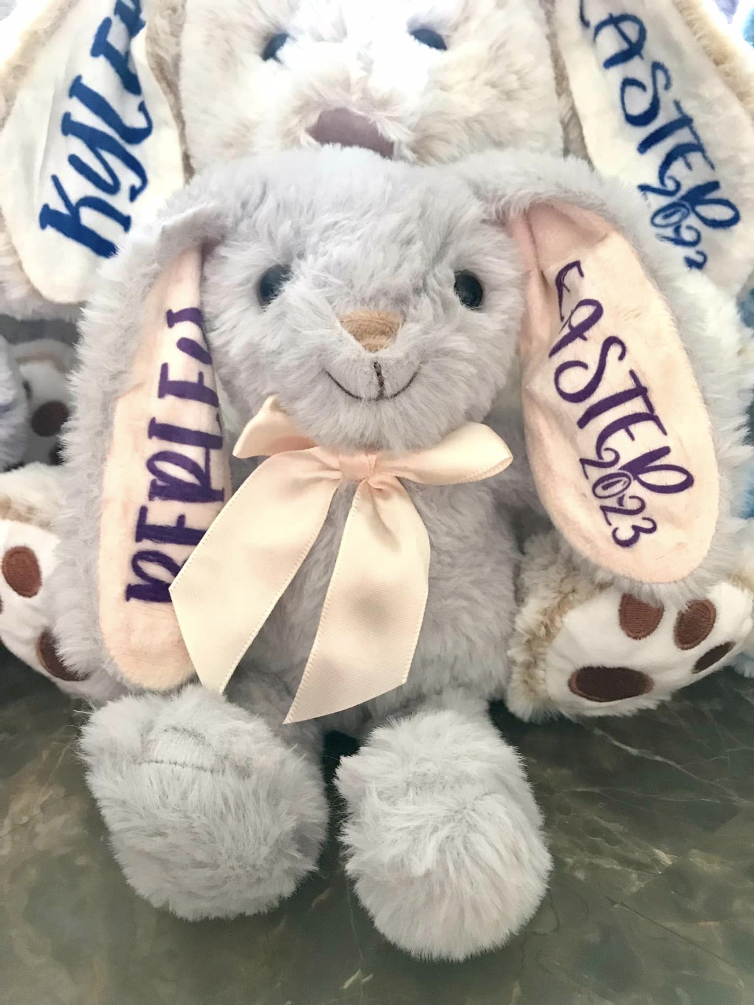 Plush bunny toy with 'Easter 2023' on ears and bow, on a reflective surface.