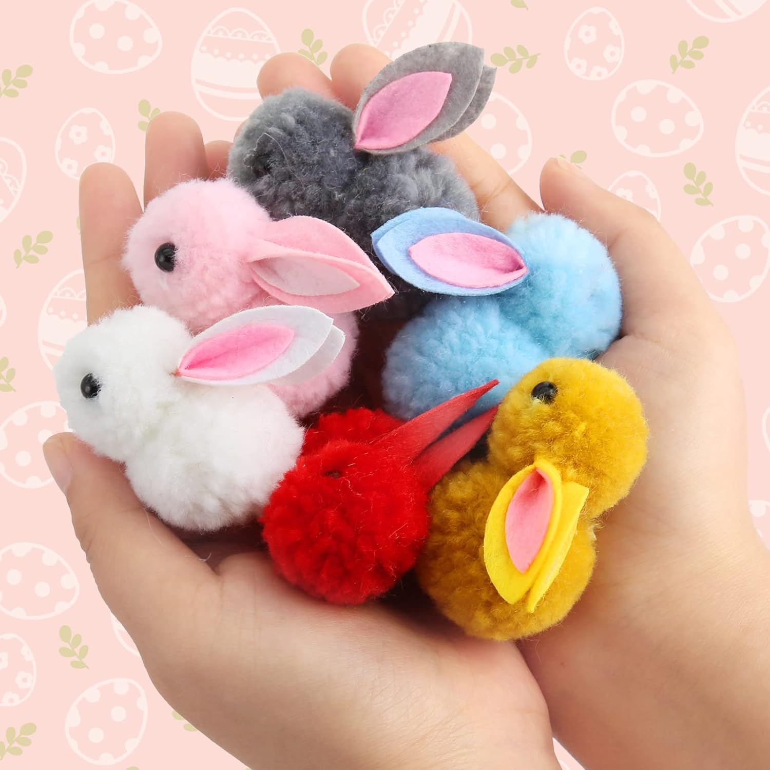 Colorful fluffy keychains shaped like bunnies held in a hand against a pink background with bunny patterns.